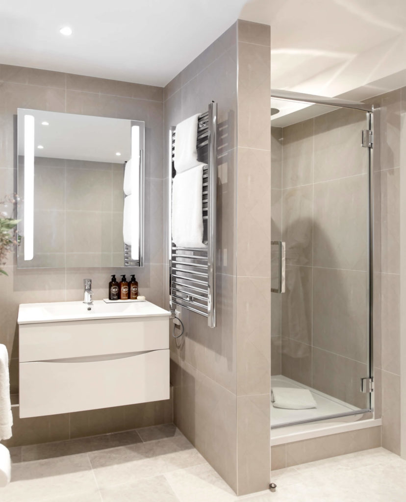 Modern bathroom with sleek shower, illuminated mirror, heated towel rack, and luxury toiletries at Arlington House Apartments.
