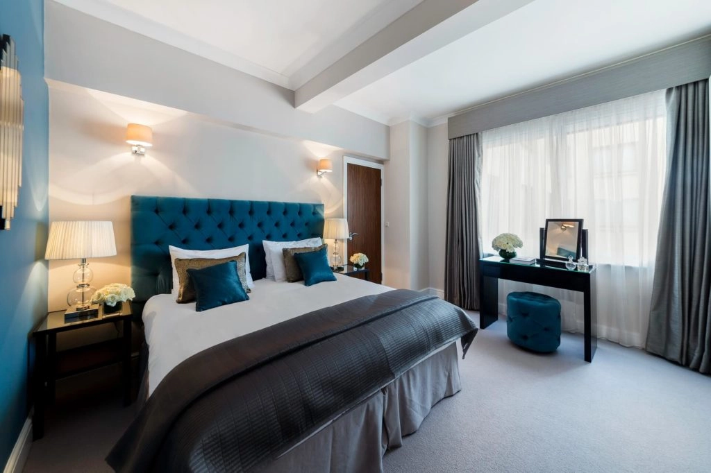 Elegant suite at Arlington House Apartments with plush bed, stylish decor, and natural light from large window.