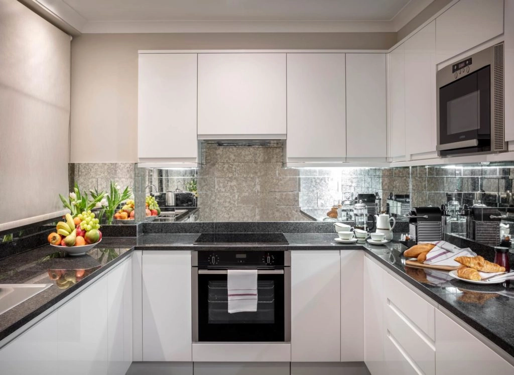 Elegant modern kitchen with sleek white cabinets, granite countertops, fresh fruit, and coffee maker at Arlington House Apartments.
