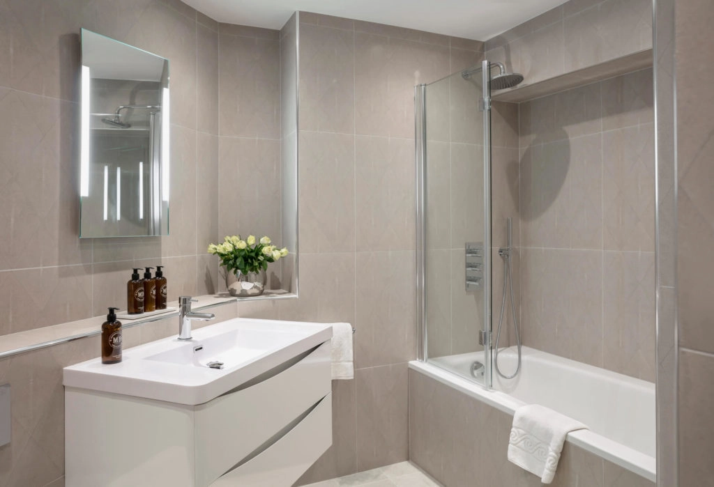 Elegant bathroom with vanity and bath, featuring modern fixtures, glass shower and fresh flowers at Arlington House Apartments.