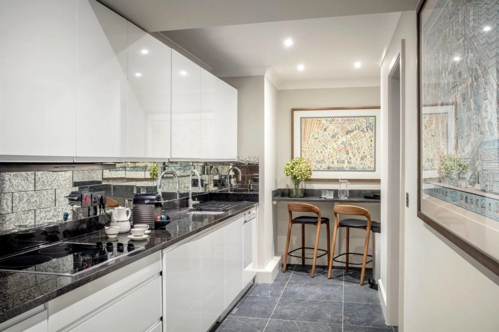 Modern kitchen in Arlington House Apartments featuring sleek white cabinets, granite surfaces, bar seating, and art decor.