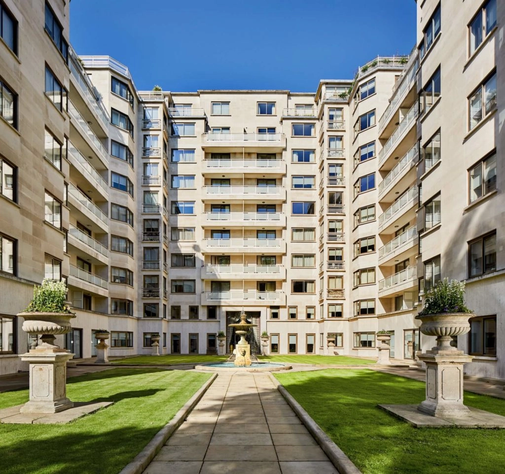 Elegant courtyard view of Arlington House Apartments, featuring lush gardens, grand architecture, and tranquil outdoor seating.