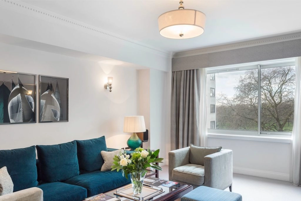Luxurious apartment lounge with plush blue sofa, elegant decor, large window view of trees in Arlington House Apartments.