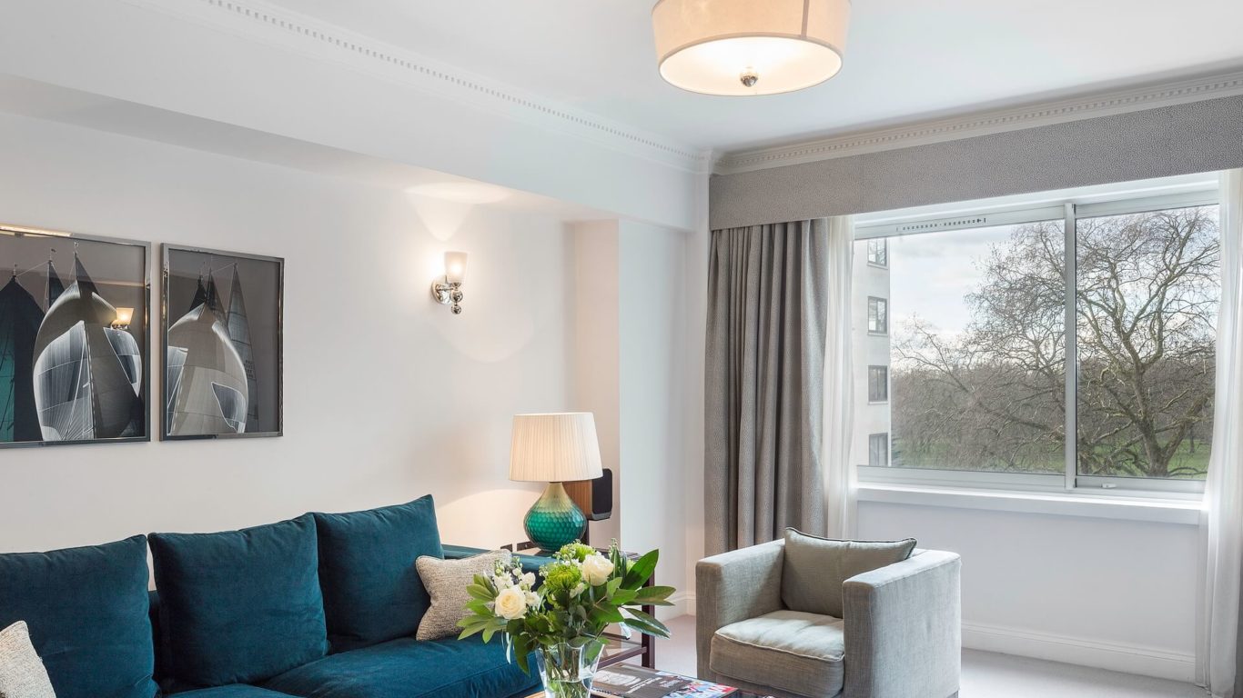 Luxurious apartment lounge with plush blue sofa, elegant decor, large window view of trees in Arlington House Apartments.