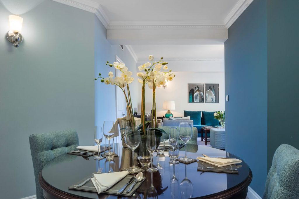 Elegant dining area with orchids, cosy seating, plush cushions, enhancing a warm, luxurious hotel stay in central London.