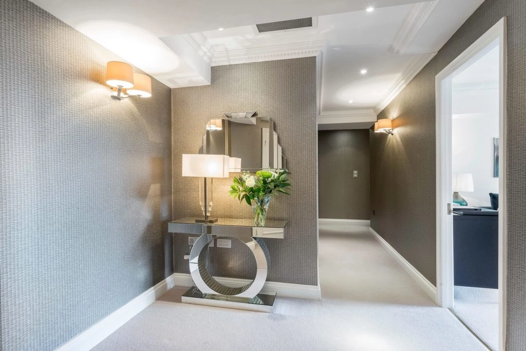 Elegant hotel corridor with chic lighting, stylish console table, mirror, and fresh flowers, offering a warm welcome.
