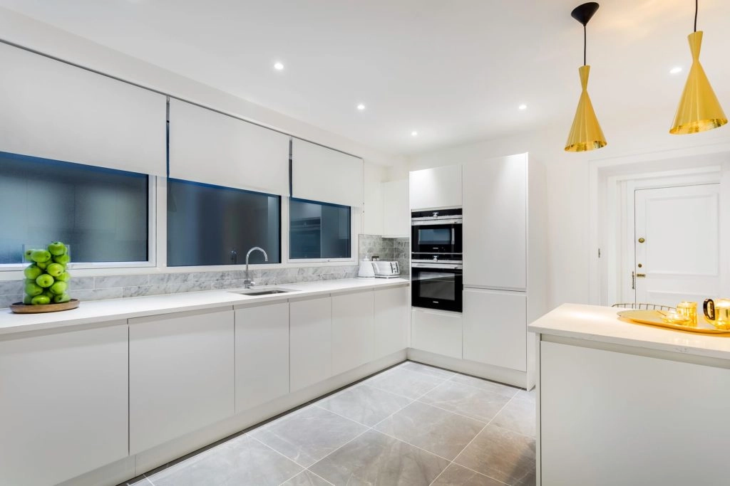 Modern kitchen in Arlington House Apartments with sleek white cabinets, integrated ovens, and elegant lighting.