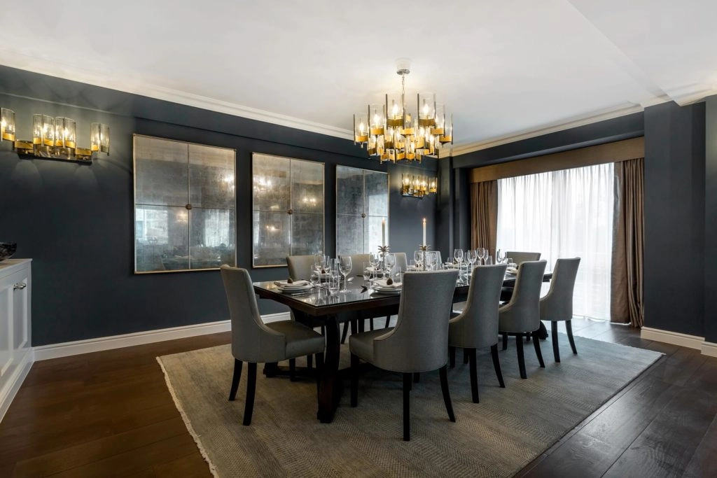 Elegant dining room with long table, plush grey chairs, modern chandelier, and large windows at Arlington House Apartments.