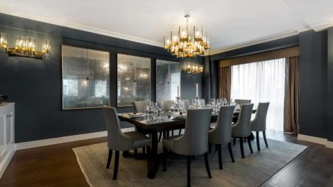 Elegant dining room with long table, plush grey chairs, modern chandelier, and large windows at Arlington House Apartments.