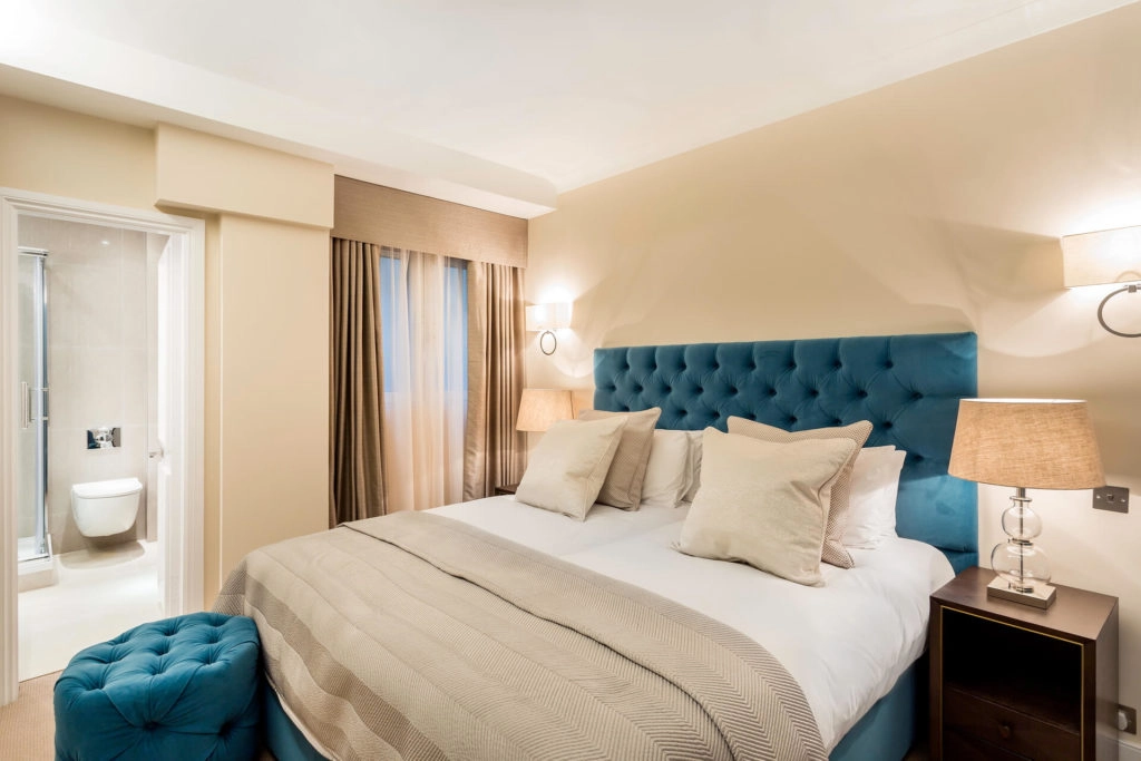 Elegant Arlington House bedroom with plush blue headboard, cosy bedding, warm lighting, and en-suite bathroom.