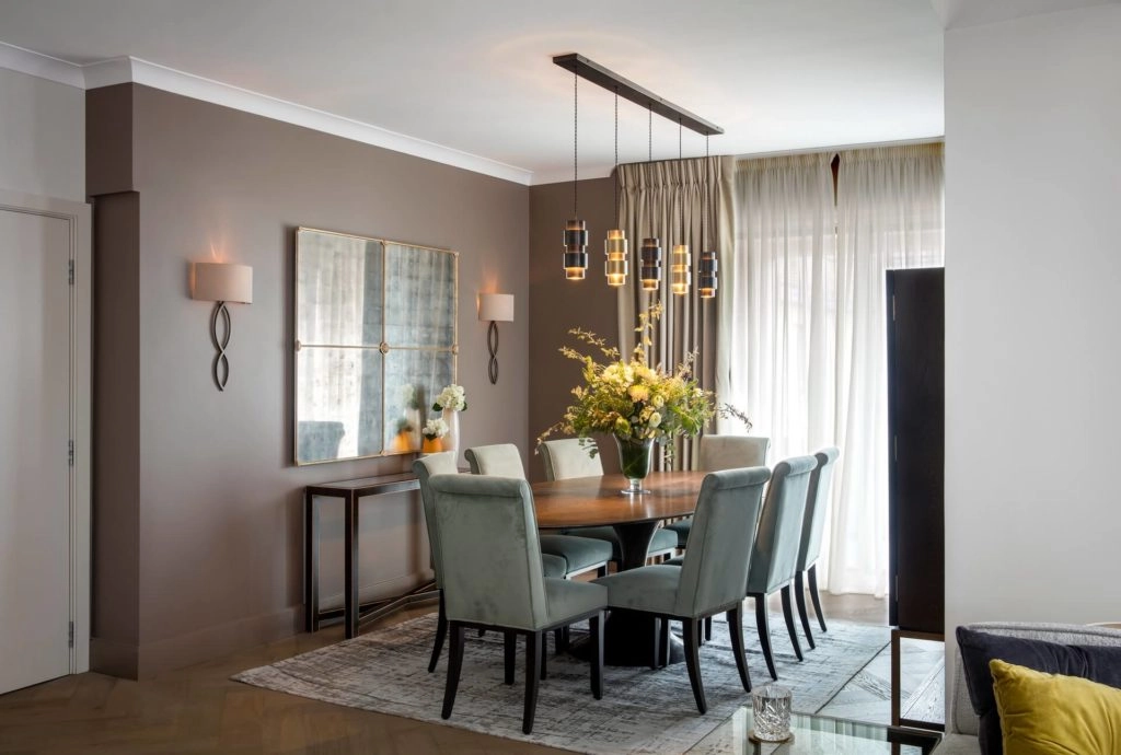 Elegant dining area with plush chairs, floral centrepiece, modern lighting, and soft natural light at Arlington House Apartments.
