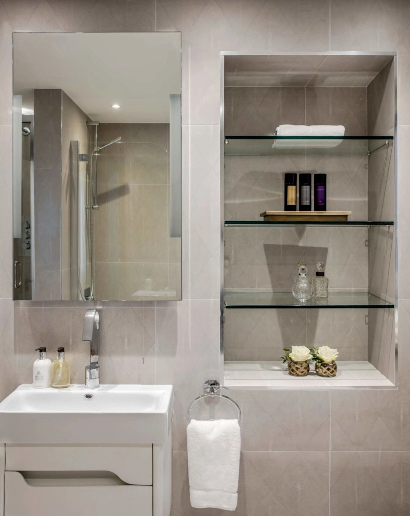 Contemporary bathroom with sleek vanity, glass shelves, luxury toiletries, fresh towels, and elegant decor at Arlington House Apartments.