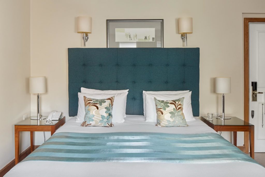 Elegant bedroom with plush double bed, teal headboard, floral cushions, and bedside lamps at Arlington House Apartments.