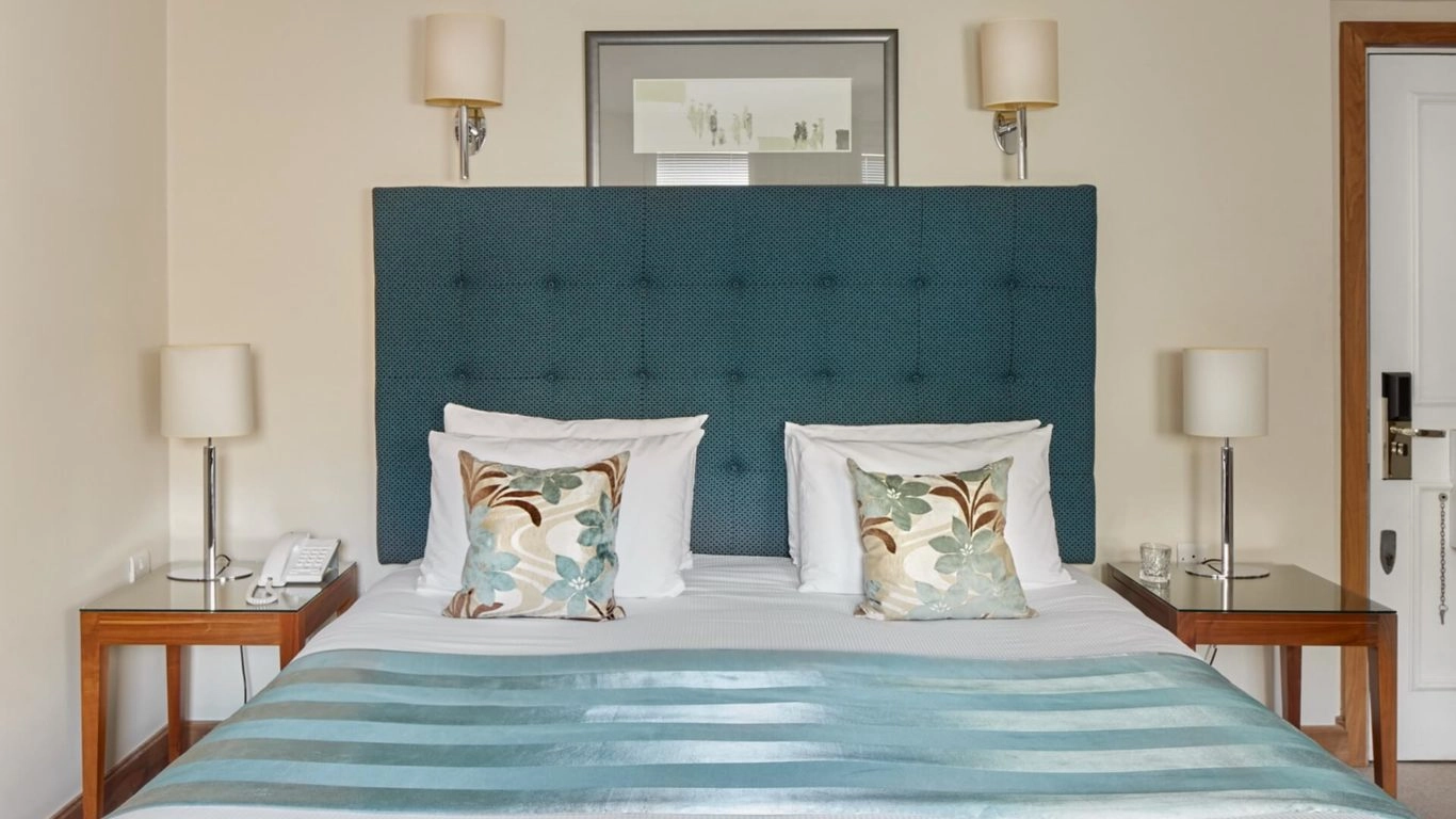 Elegant bedroom with plush double bed, teal headboard, floral cushions, and bedside lamps at Arlington House Apartments.