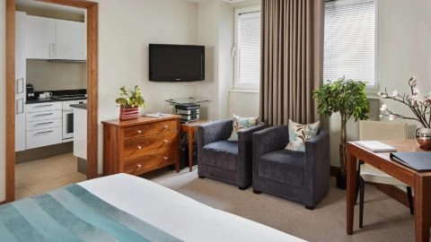 Cosy apartment with plush chairs, kitchen, flat-screen TV, and elegant decor at Arlington House Apartments.