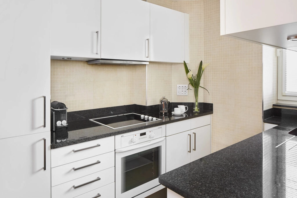 Modern kitchen with sleek white cabinets, black countertops, induction hob, and coffee setup at Arlington House Apartments.