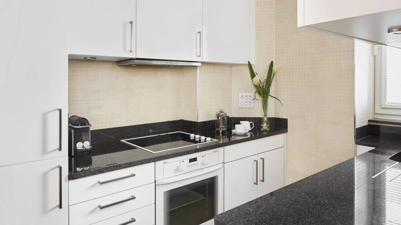 Modern kitchen with sleek white cabinets, black countertops, induction hob, and coffee setup at Arlington House Apartments.