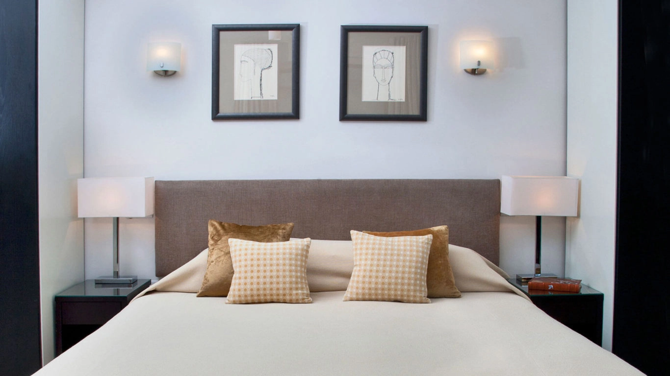 Elegant bedroom with plush pillows, modern lamps, and framed artwork at Arlington House Apartments, offering a cosy retreat.