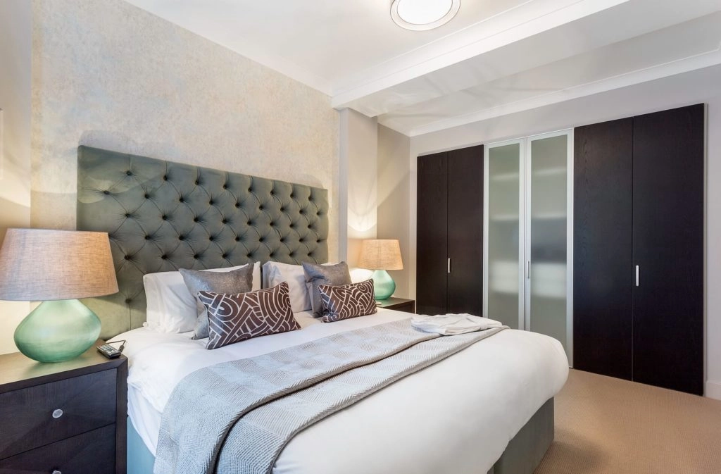 Elegant hotel bedroom with plush bed, stylish headboard, warm lighting, spacious wardrobe, inviting and comfortable ambiance.