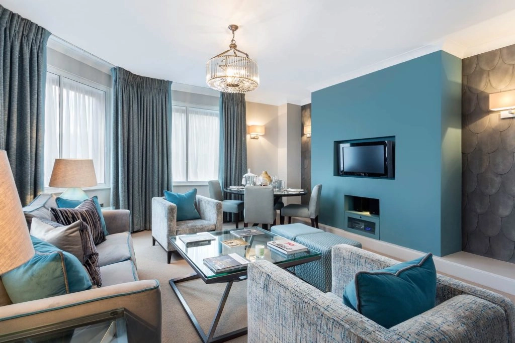 Elegant apartment lounge with plush sofas, teal accents, flat-screen TV, and dining area; ideal for a luxurious London stay.