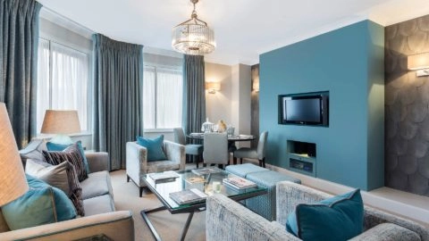 Elegant apartment lounge with plush sofas, teal accents, flat-screen TV, and dining area; ideal for a luxurious London stay.