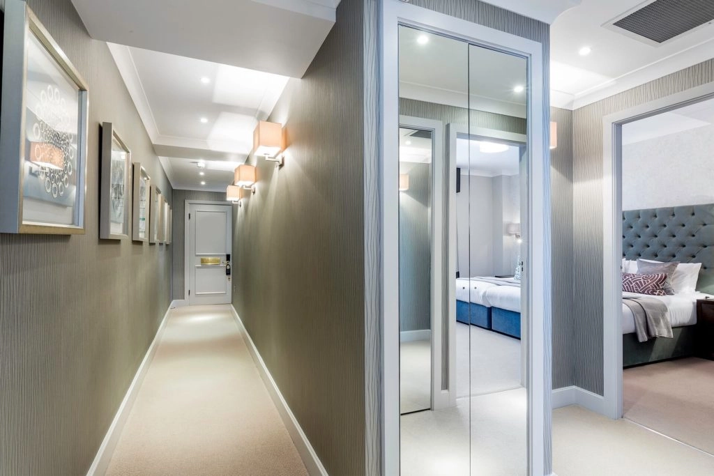 Spacious hallway leading to elegant suite with plush bedding, mirrored doors, cosy lighting. Experience luxury at Arlington House.